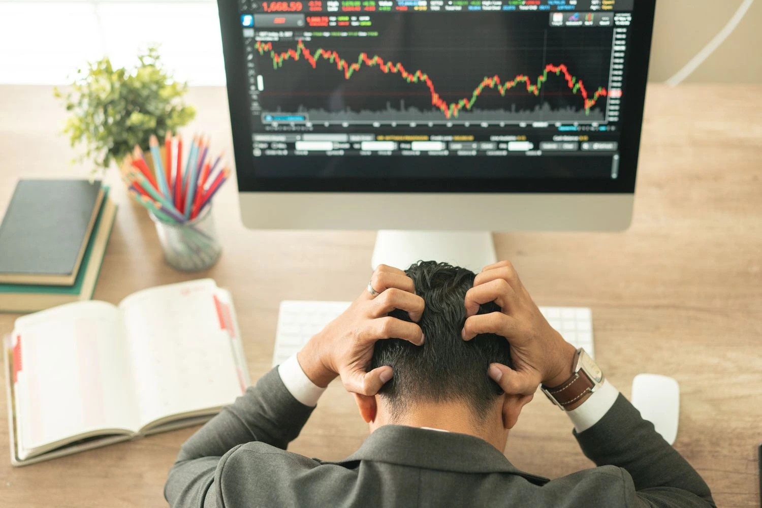 1. A person in business attire sitting at a desk, holding their head in frustration while looking at a stock market chart on a computer screen.